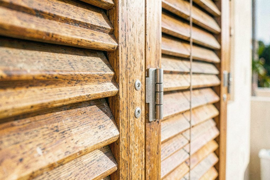 Teak louvered shutter with a stainless steel hinge, by the sea