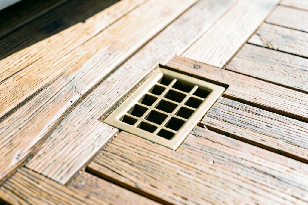 Weathered teak decking and brass drain grate in bright sunlight