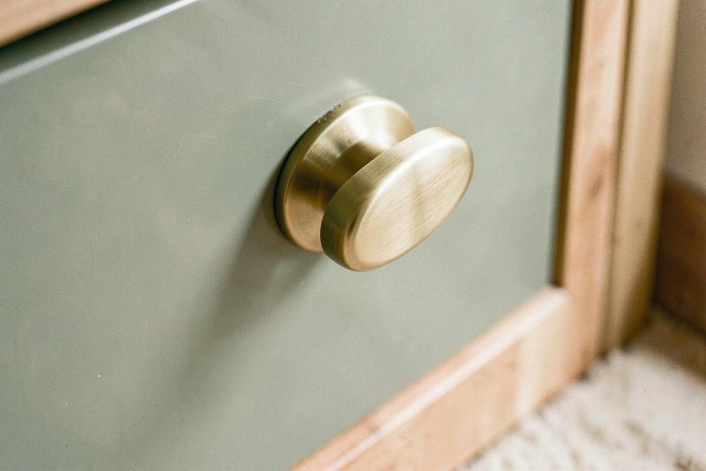 Brushed brass handles on matte sage green lacquer cabinet surface